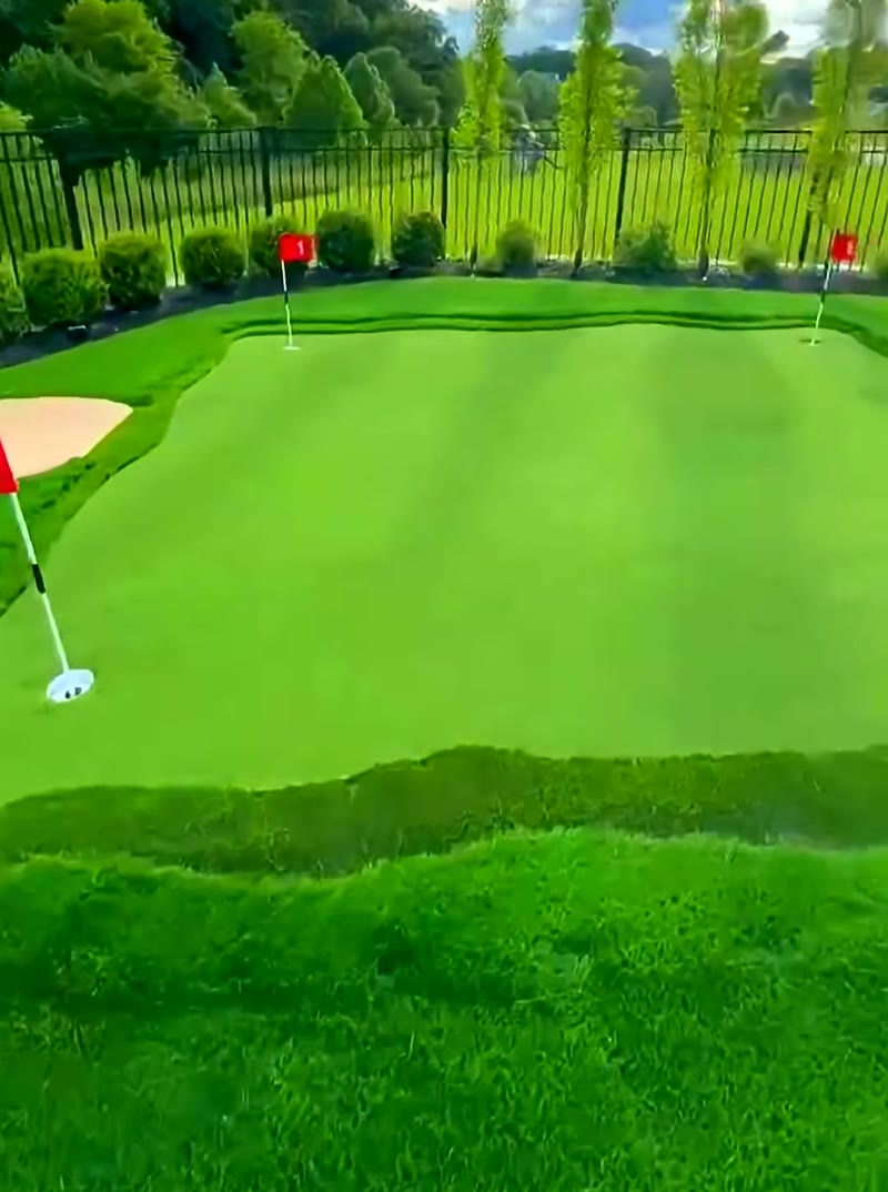 Backyard putting green with sand bunker, red flags, and estate fencing in Central NJ