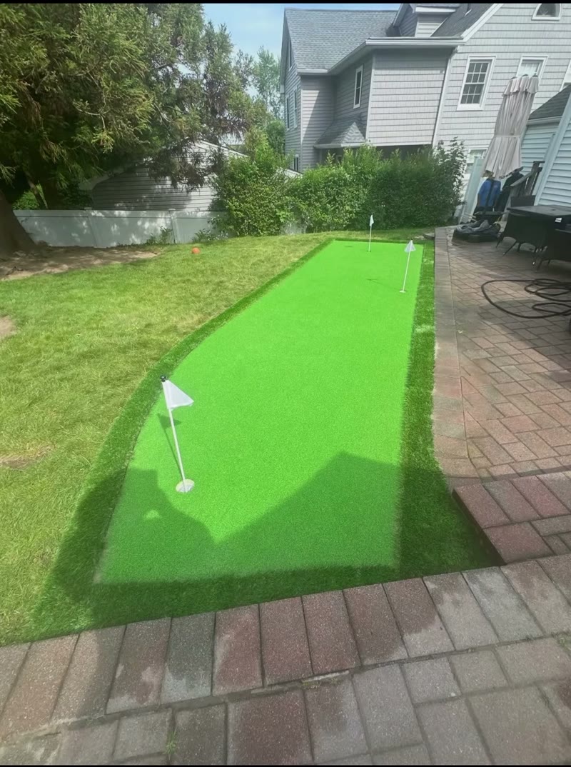 Compact backyard putting lane with two cups beside a brick paver patio