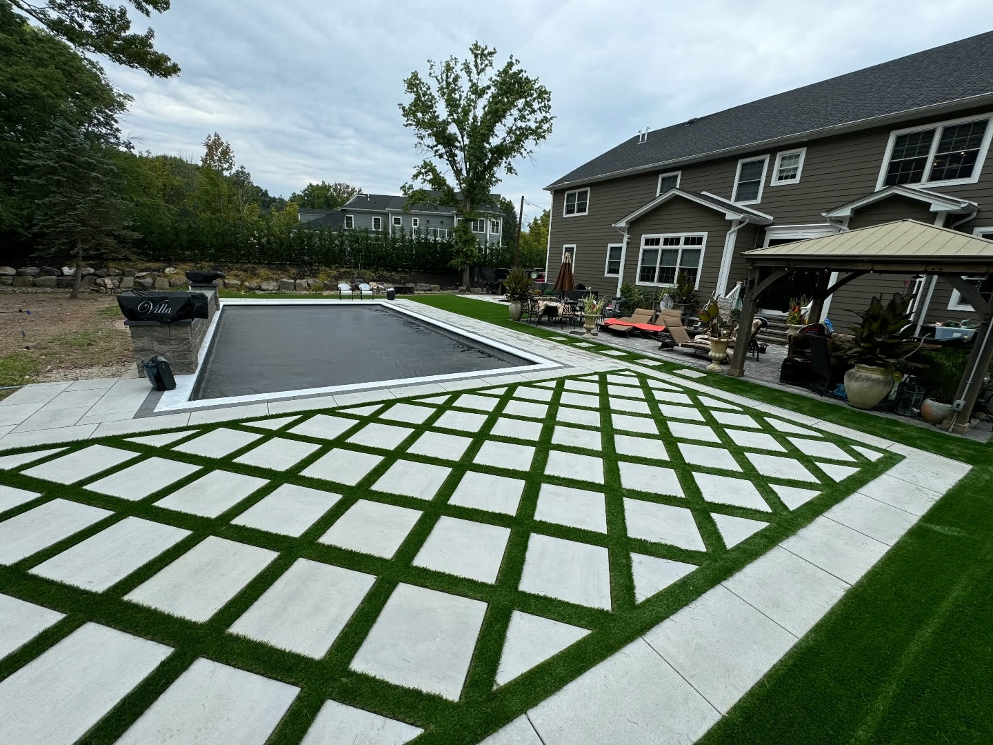 Large-format pavers set in a synthetic turf grid wrapping a pool deck in Old Bridge, NJ, with gazebo and outdoor kitchen