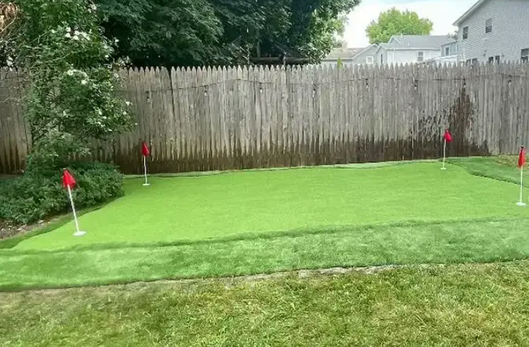 Custom backyard synthetic putting green with multiple flagged holes and contoured turf